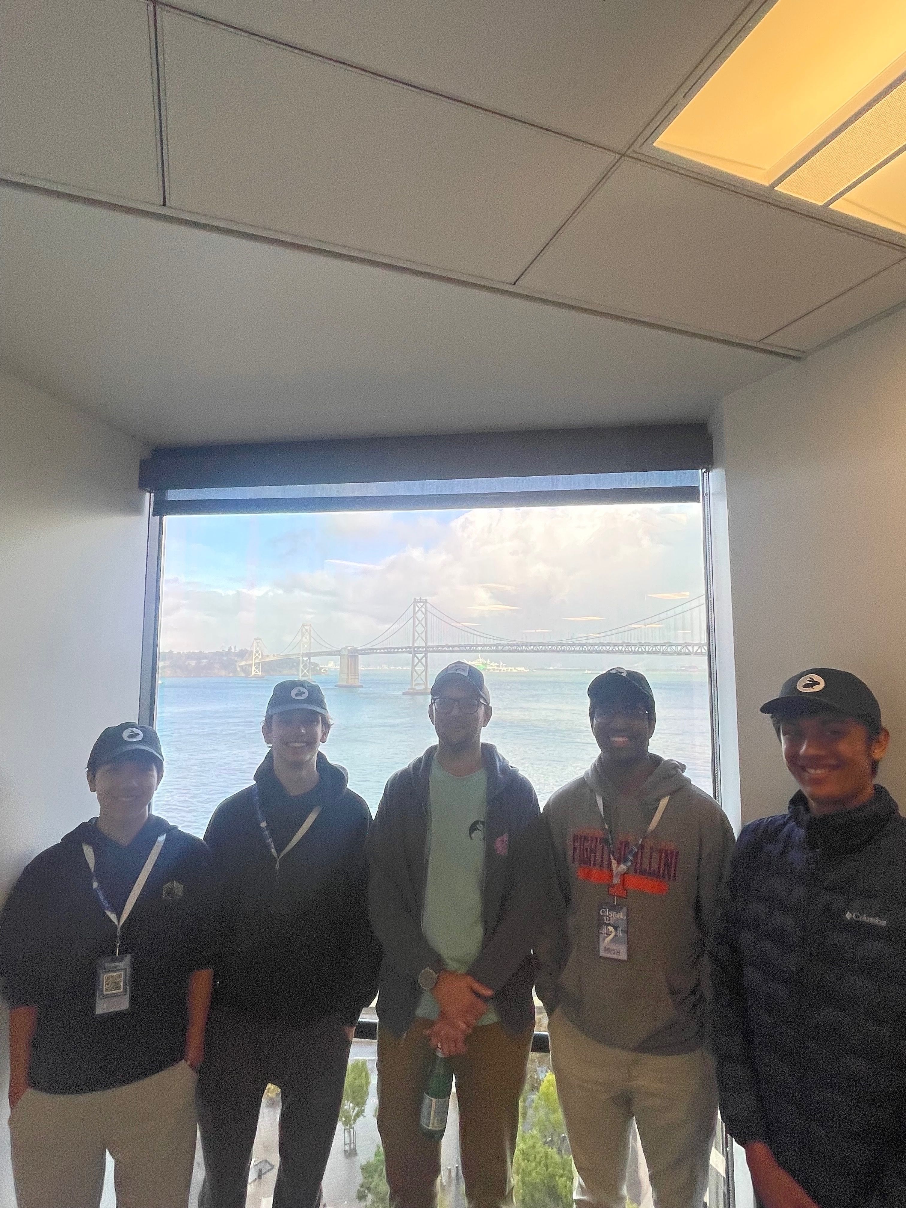 Five men stand by a large window overlooking a body of water and the distant horizon.