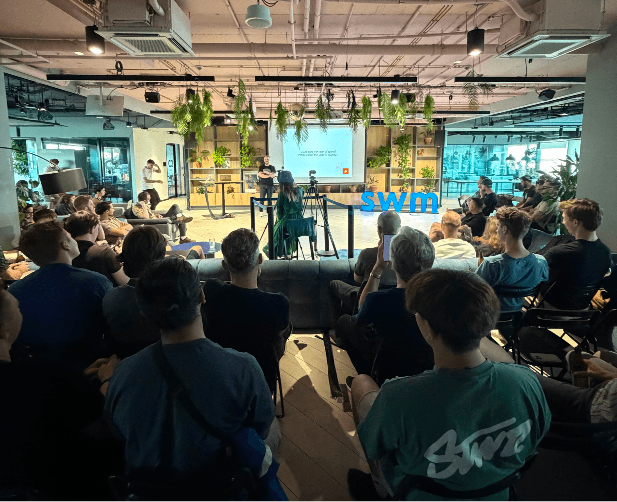 Audience attending a tech presentation with a speaker on stage and a 'swim' logo.