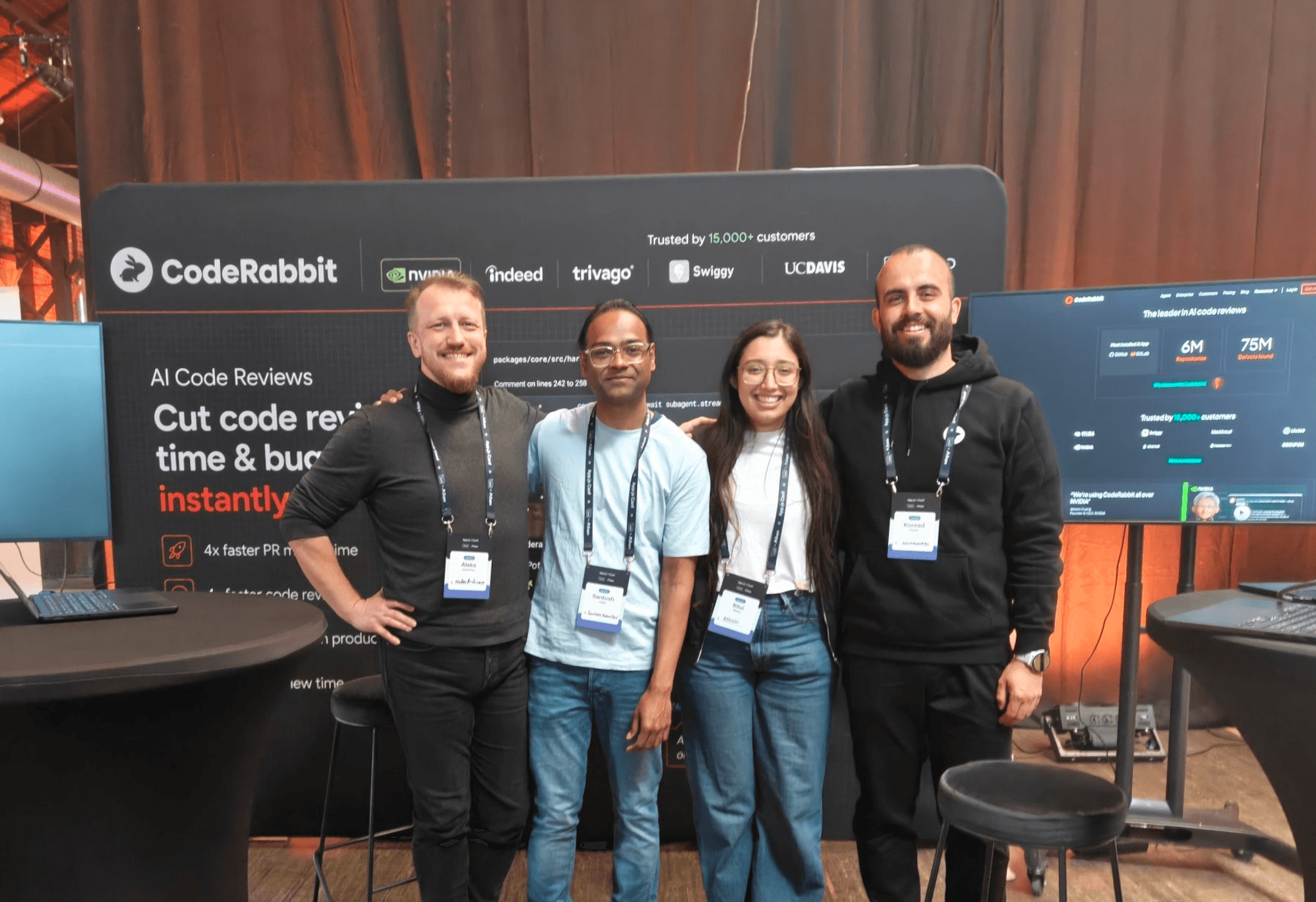 Four smiling team members stand by the CodeRabbit AI code review booth at an event.